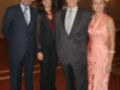 Una familia posa juntos en un ambiente formal, con dos hombres vestidos con trajes y una mujer con un vestido de gala. La escena parece ser en un evento o recepción, posiblemente una celebración familiar.