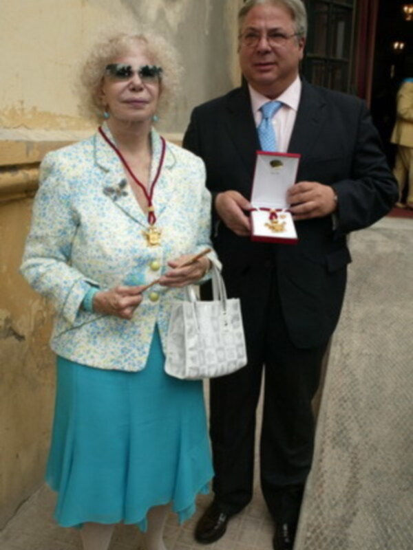 Una pareja elegante posa con una medalla y un certificado en un evento formal.
