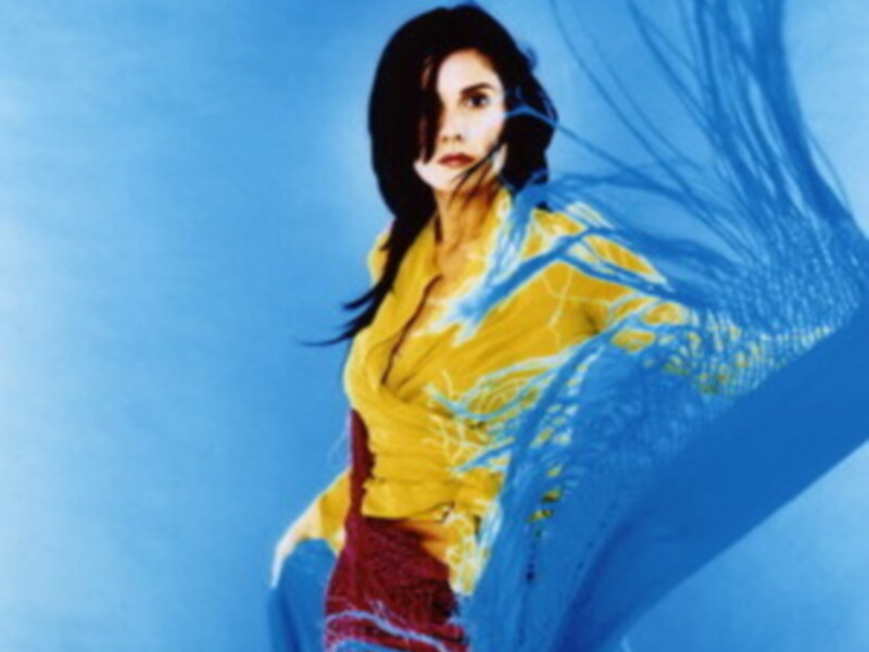 Una mujer con cabello largo y rojo, vestida con una camisa amarilla brillante y pantalones rojos, se encuentra nadando en aguas azules. La imagen tiene un estilo de arte digital con líneas y colores vibrantes que dan vida a la escena.