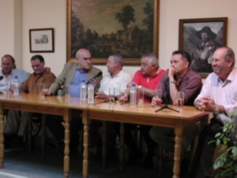 Un grupo de personas sentadas en una mesa, con pinturas en el fondo.