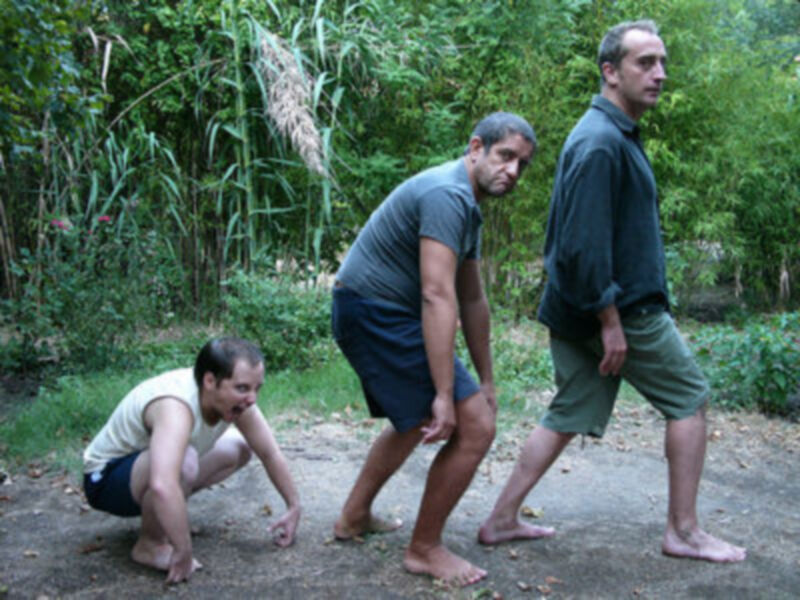 Tres hombres en un entorno natural, uno arrodillado y los otros dos en posición de pie, interactuando con el suelo.