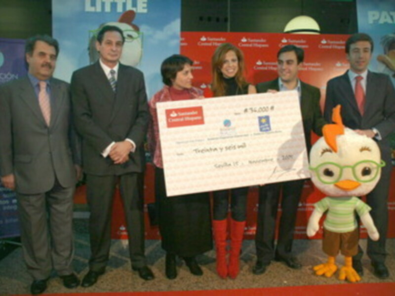 Una celebración de premios con un personaje de dibujos animados en el centro, rodeado de personas en trajes formales, con un fondo que incluye un cartel con el nombre 'Little' y un personaje de dibujos animados en la parte superior derecha.