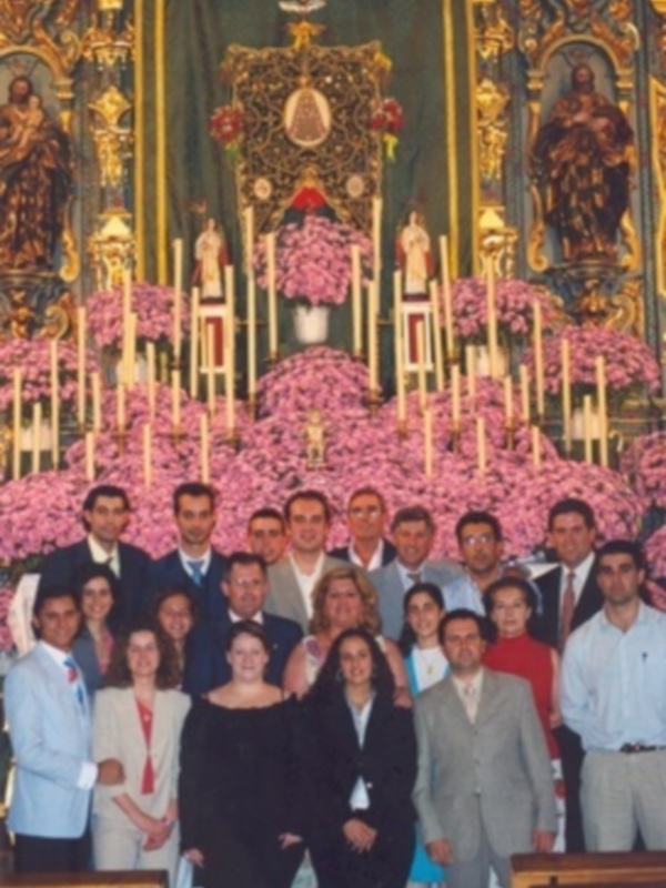 Una reunión formal en una iglesia, con una gran imagen de la Virgen en el fondo y una mesa con flores en el centro.