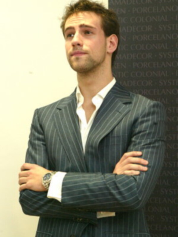 Hombre con traje de pana a rayas, brazos cruzados, fondo con texto repetido de 'Porcelanosa'.