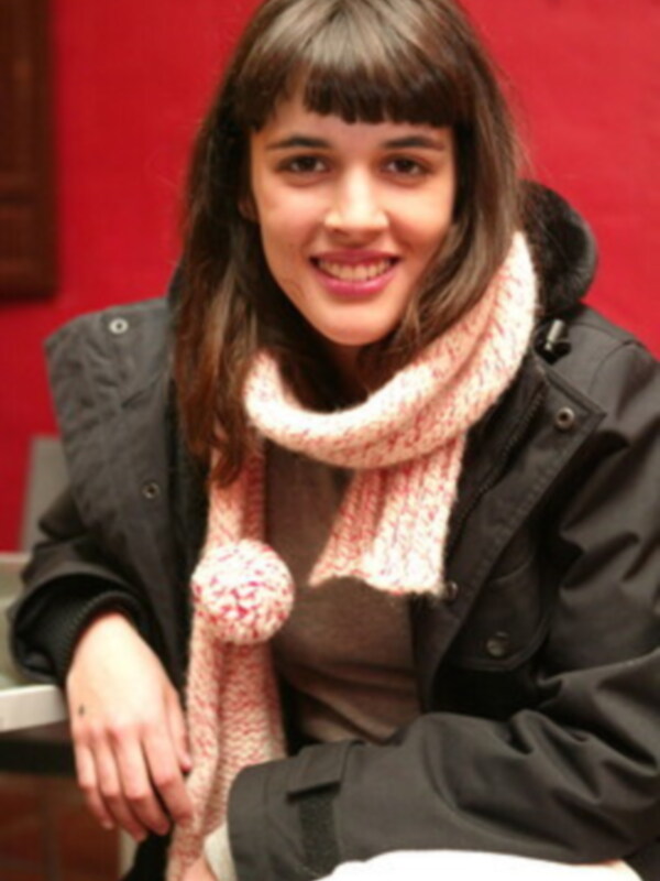 Persona sonriente con bufanda de punto y abrigo negro, fondo rojo.