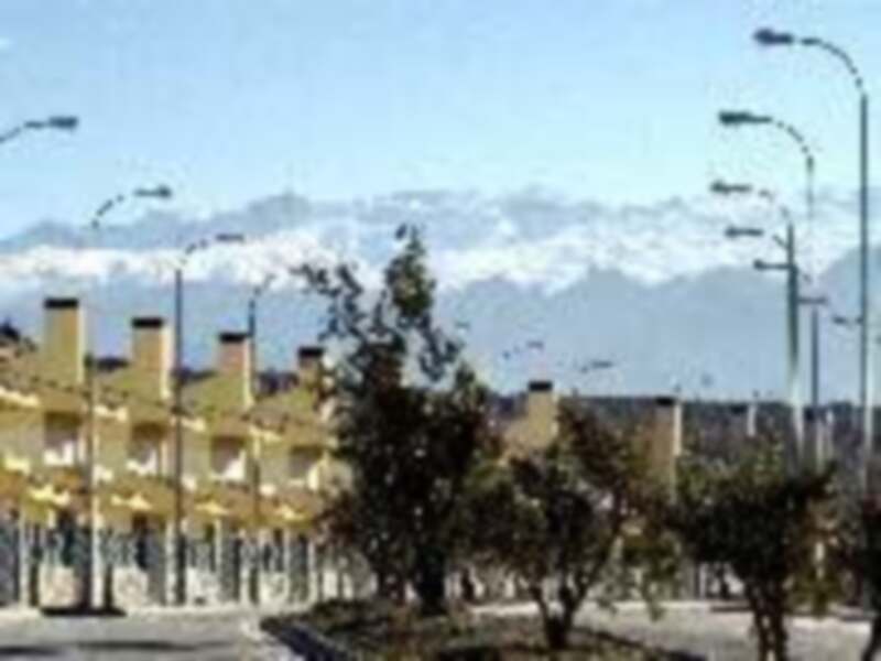 Imagen de una ciudad con edificios y árboles, en el fondo se ven montañas nevadas.
