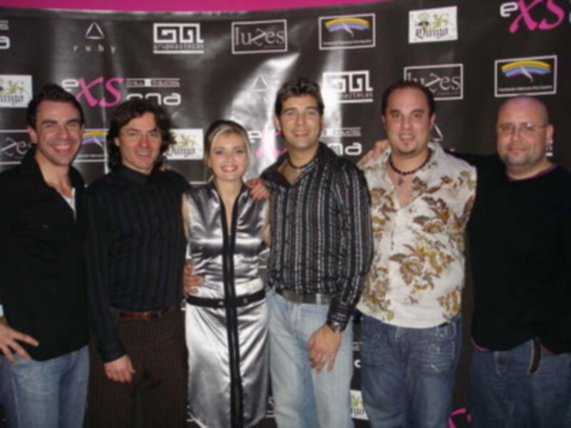 Grupo de personas posando juntos en un evento con carteles de patrocinadores en el fondo.