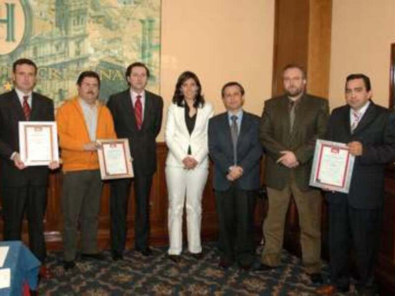 Una reunión formal en un entorno oficial, con personas vestidas formalmente, posando para una foto de grupo, sosteniendo certificados. El ambiente es formal y la decoración incluye elementos de estilo clásico.