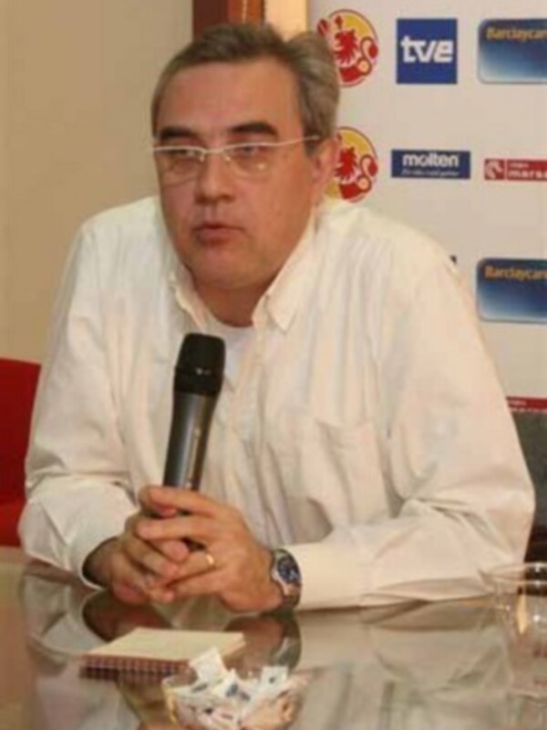 Un hombre con gafas y una camisa blanca está sosteniendo un micrófono, frente a un fondo con logos de empresas.