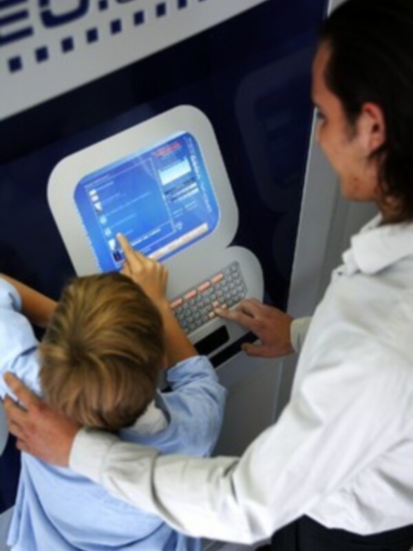 Una persona y un niño interactúan con una pantalla táctil de un equipo de cajero automático.