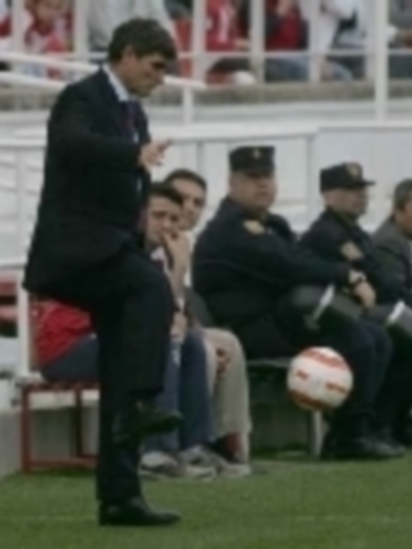 Entrenador en acción durante un partido de fútbol en un estadio con público en la grada.