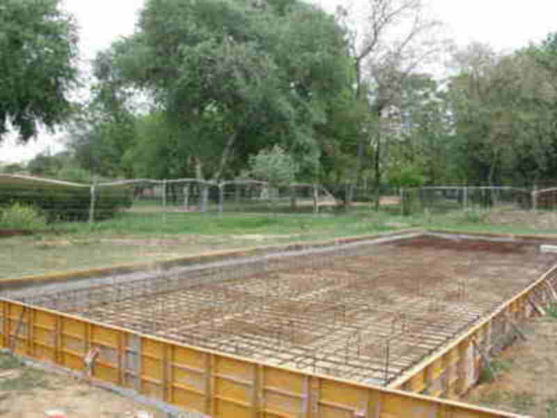 Un terreno en construcción con una base de hormigón listo para la fundación, rodeado de vegetación y un cercado.