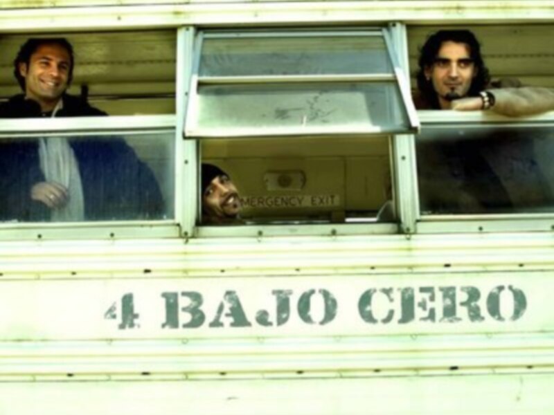 Tres personas sonrientes asomándose por las ventanas de un autobús con el texto '4 BAJO CERO' en la parte inferior.