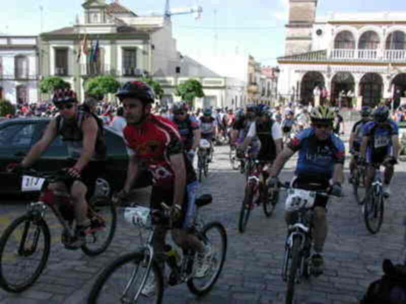 Bicicletas en una carrera urbana, gente en bicicleta, edificios coloniales y banderas.