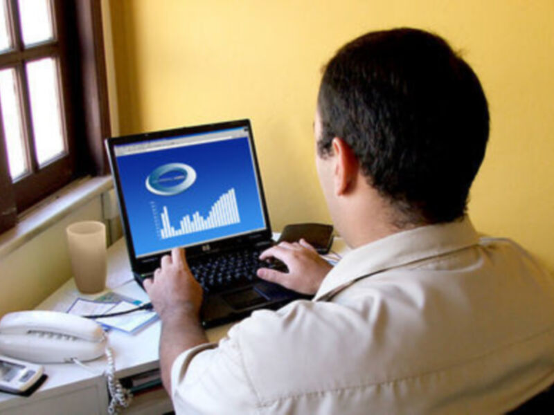 Persona trabajando en un ordenador portátil con gráficos en la pantalla, en un entorno de oficina con una ventana al lado.