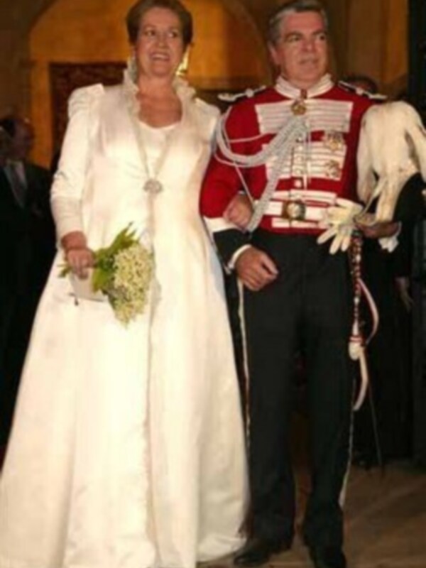 Novios elegantes en traje de boda y uniforme militar, sosteniendo un ramo de flores.