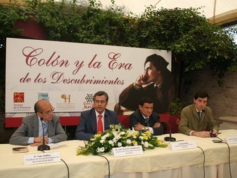 Conferencia sobre Colón y la Era de los Descubrimientos en un evento formal con paneles y flores.