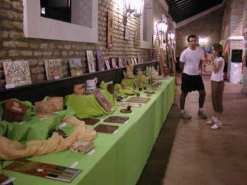 Exposición de artesanía en un espacio interior con mesas llenas de productos artesanales y visitantes.