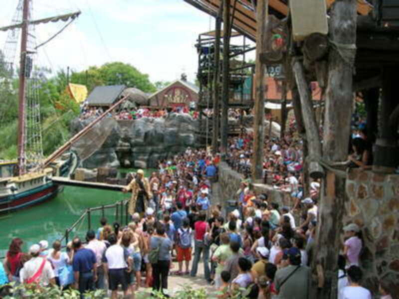 Una multitud de personas disfruta de un emocionante show en un parque temático, rodeadas por estructuras de madera y agua.