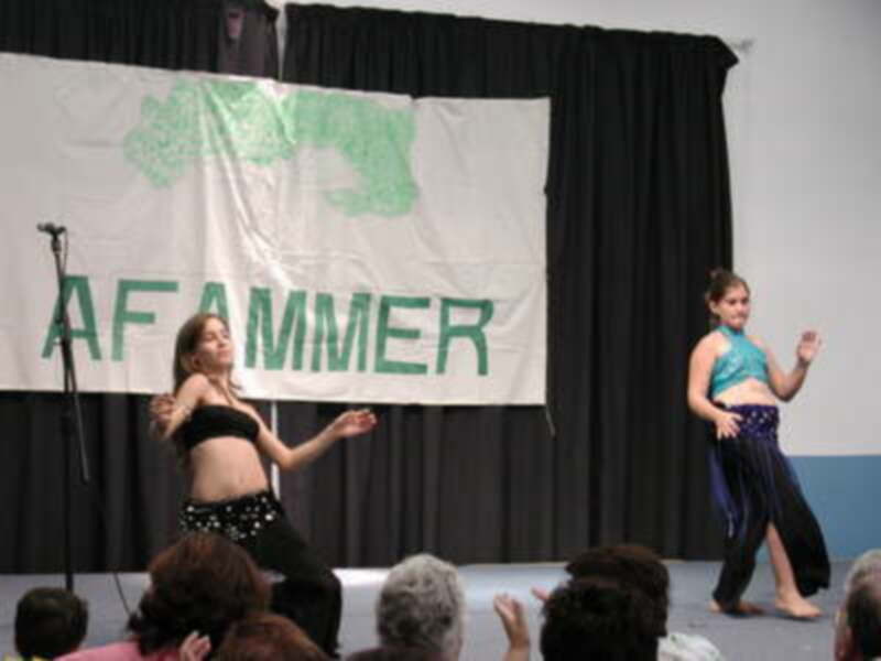 Dos bailarinas en un escenario frente a una bandera que dice "AFAMMER".