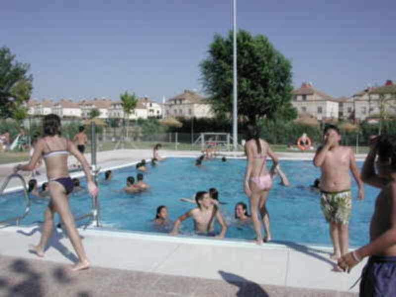 Piscina pública con personas disfrutando del agua bajo un cielo azul claro.