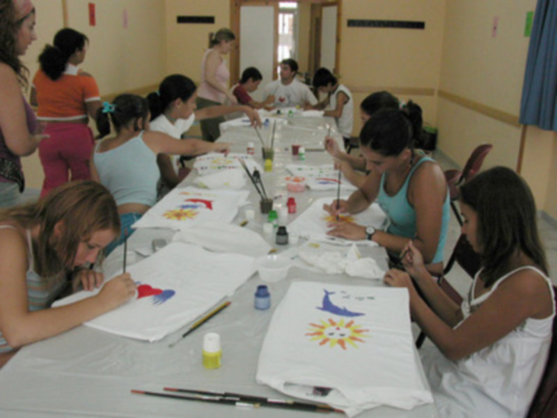 Una clase de pintura en un aula con estudiantes trabajando en sus tareas, usando pinceles y pinturas de colores.