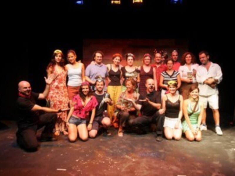 Una escena teatral con un grupo de actores y actrices posando para una foto en el escenario.