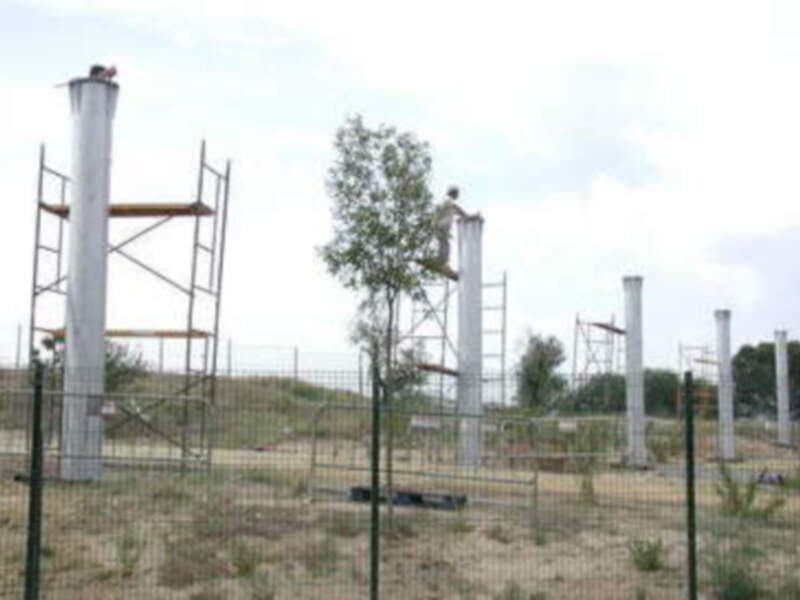 Un campo de fútbol con una valla, un árbol y estructuras de metal en el fondo.