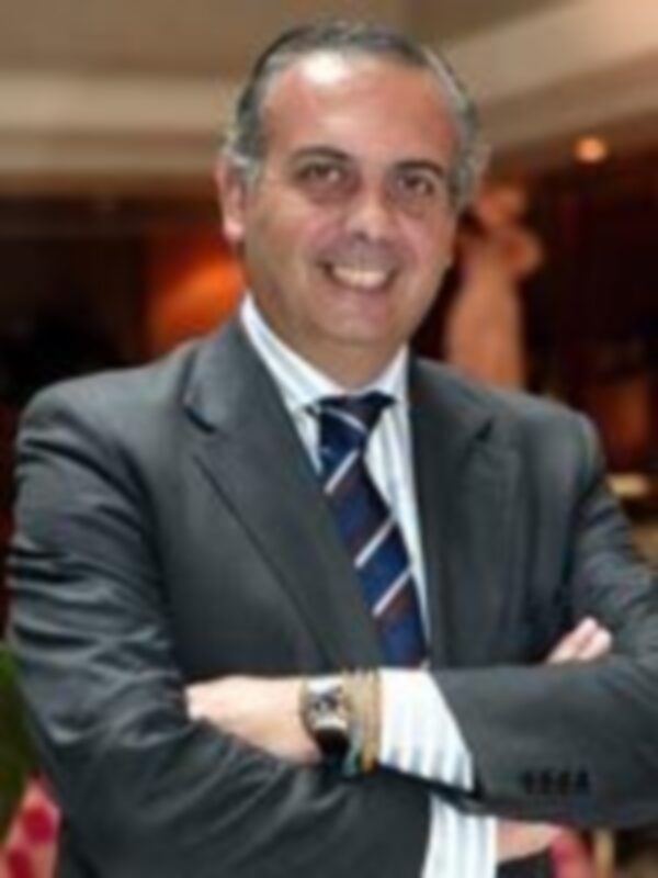 Un hombre con una camisa blanca y un corbata azul, posando con los brazos cruzados en una sala de conferencias.