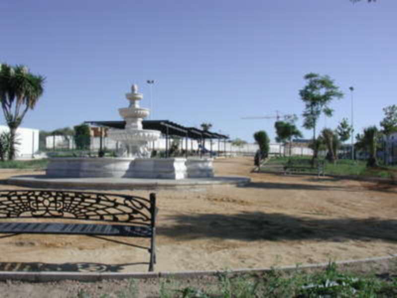 Fuente de agua en un parque con bancos y árboles alrededor.