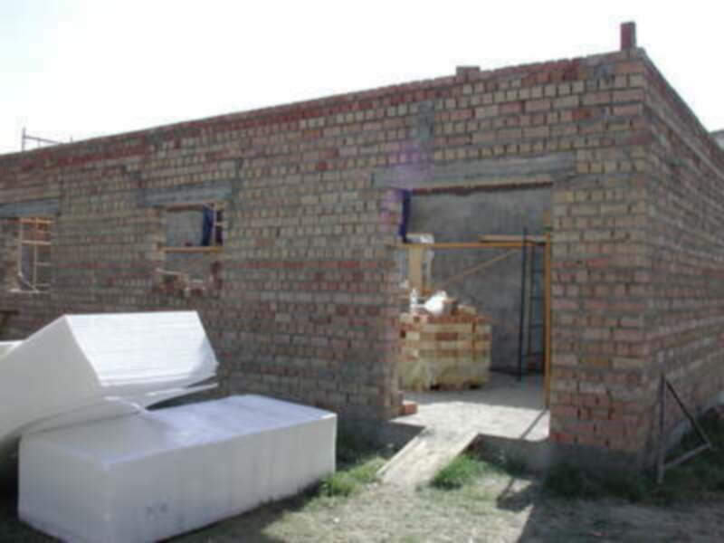 Un edificio en construcción con paredes de ladrillo y una puerta abierta. En el primer plano, hay una estructura blanca que parece ser una cama o un sofá.
