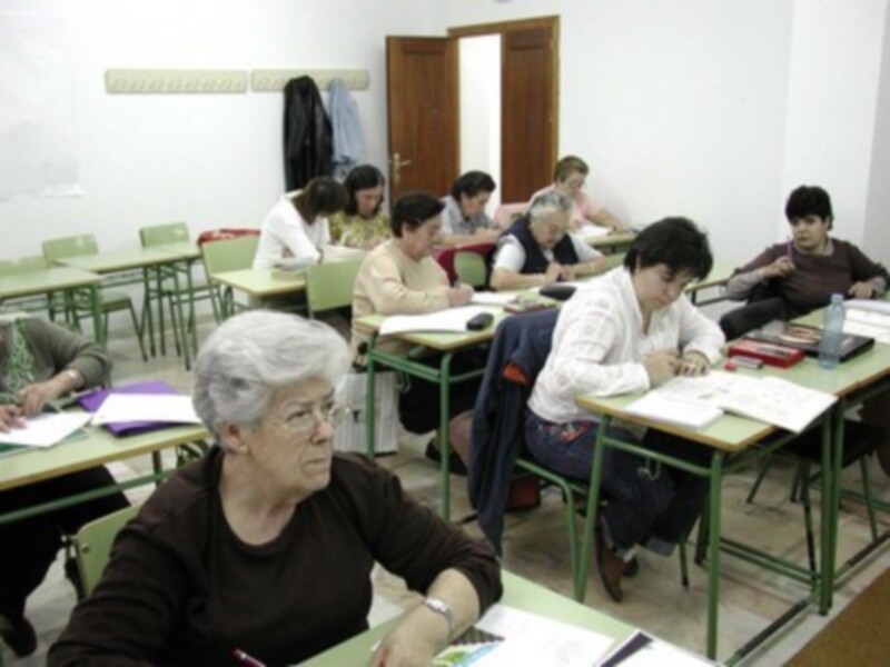 Clase de aprendizaje en un aula con estudiantes sentados en sus mesas, trabajando en sus tareas.