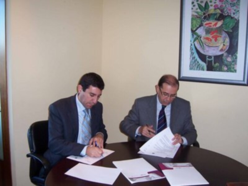 Dos hombres en traje firmando documentos en una oficina.