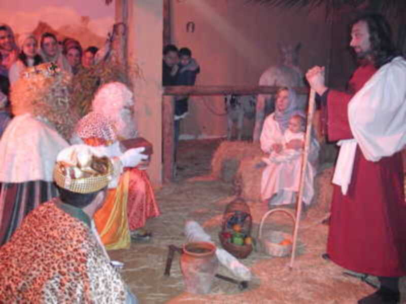 Representación de la Natividad con figuras vestidas en ropa tradicional, en un escenario con paja y elementos de la escena de la adoración de los Reyes Magos.