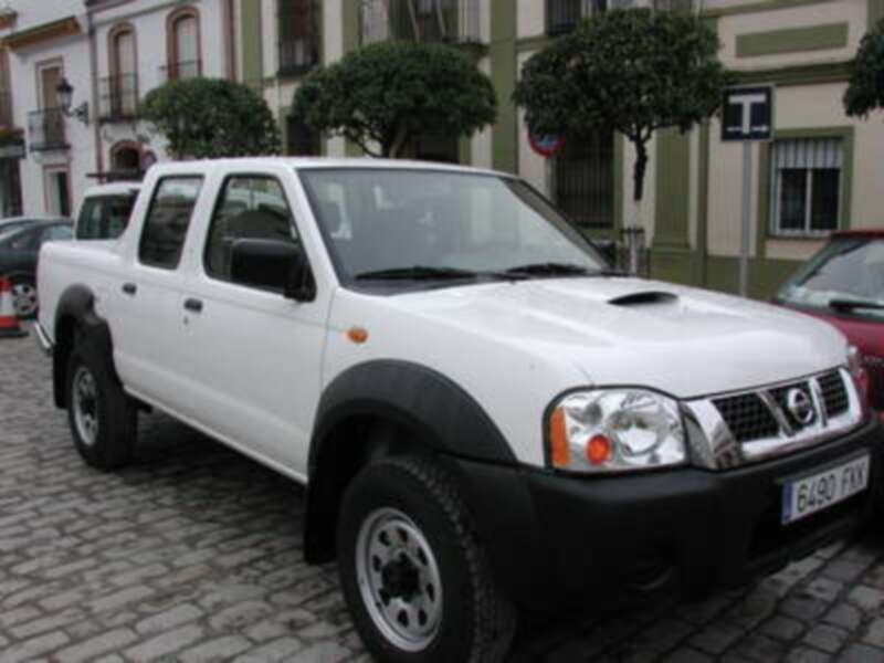 Vehículo blanco de Nissan, estacionado en una calle con edificios al fondo.