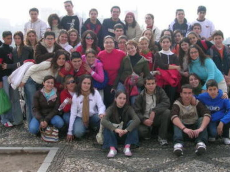 Estudiantes en un grupo, posando para una foto. Algunos llevan libros y otros sonríen. La imagen parece ser de un colegio o universidad.