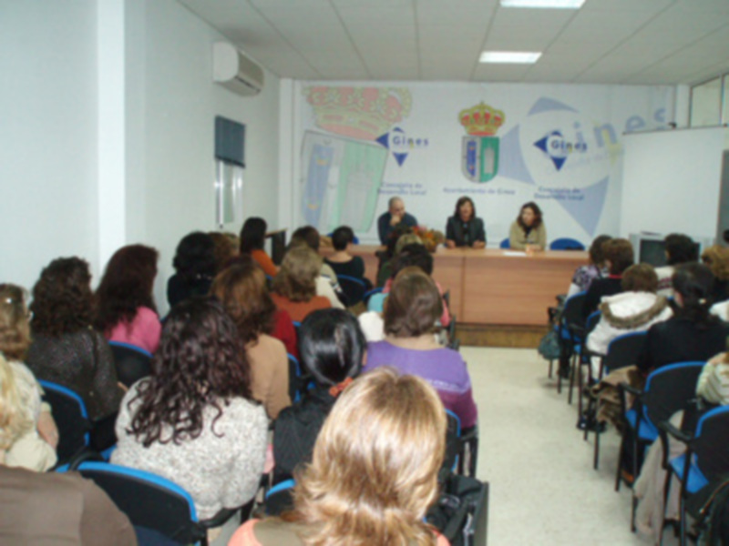 Una sala de conferencias con asistentes sentados en sillas alrededor de una mesa. La pared trasera muestra un mapa y la bandera de la ciudad.