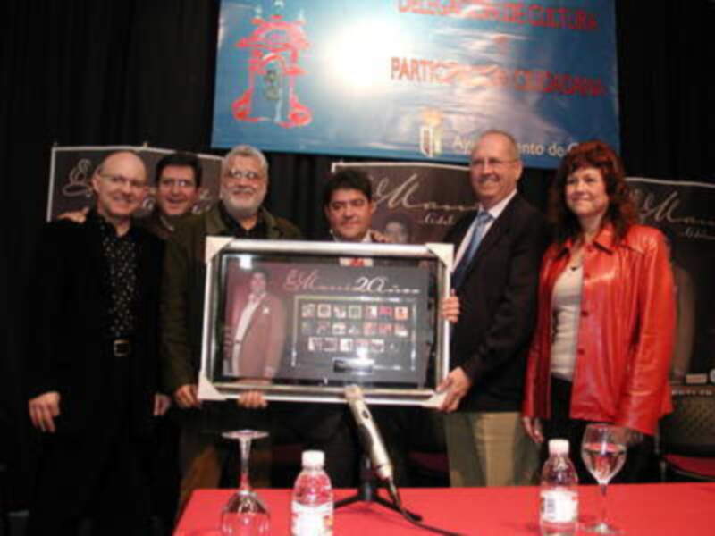 Una persona sostiene un marco con una imagen de un robot y texto, mientras otros tres personas lo observan. En el fondo, se puede ver una pancarta que dice "Participación en Chronorama".