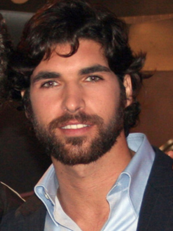 El actor Adrien Grenier sonríe con una camisa azul y una chaqueta de rayas negras.