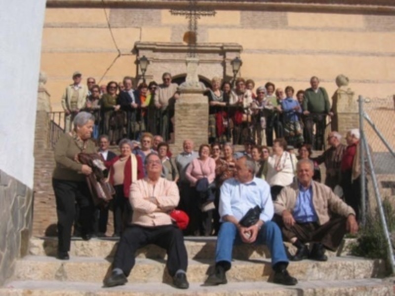 Una multitud de personas, incluyendo ancianos y jóvenes, se reúne en una escalera frente a un edificio histórico. La escena está iluminada por faroles, creando una atmósfera festiva.