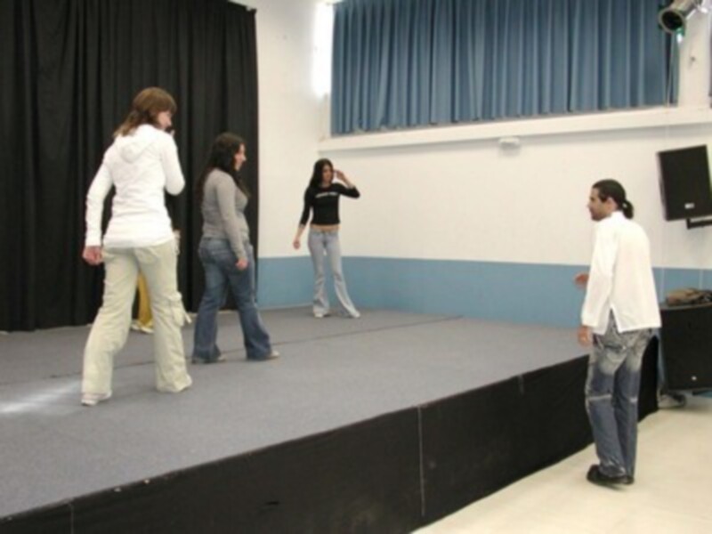Personas en una escena de teatro, dos mujeres y un hombre caminan por el escenario. La imagen muestra una escena de teatro con personas caminando en un escenario.