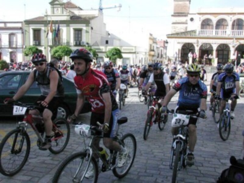 Ciclistas en una carrera de bicicletas, con edificios históricos y gente observando.