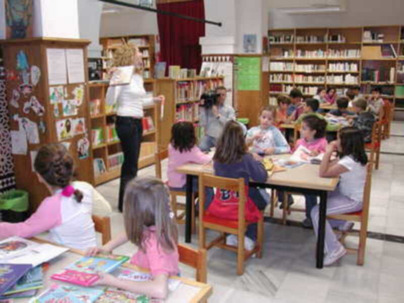 Niños en una biblioteca, con libros y juguetes. Una maestra les enseña.