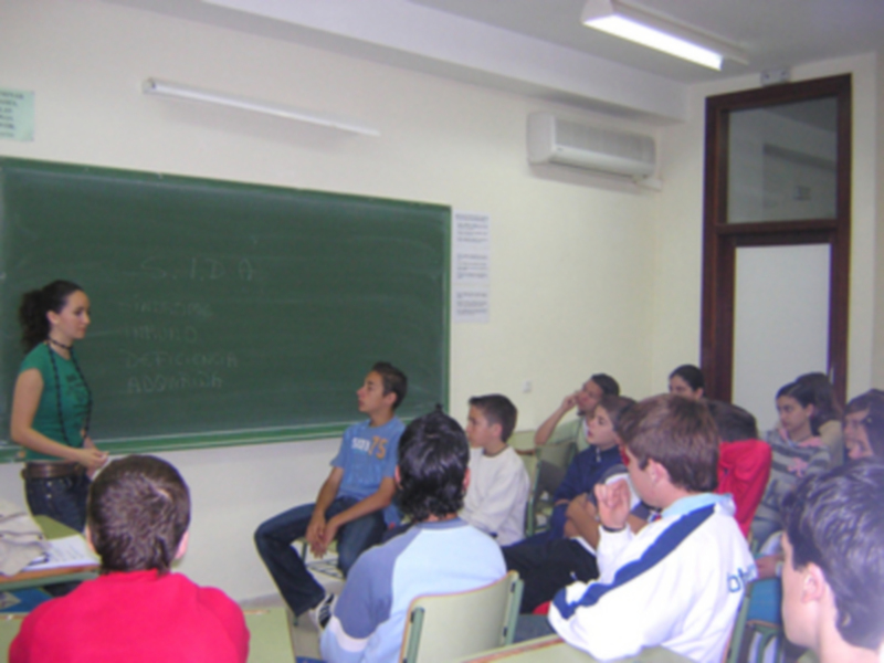 Clase en una aula con un estudiante explicando mientras otros escuchan.