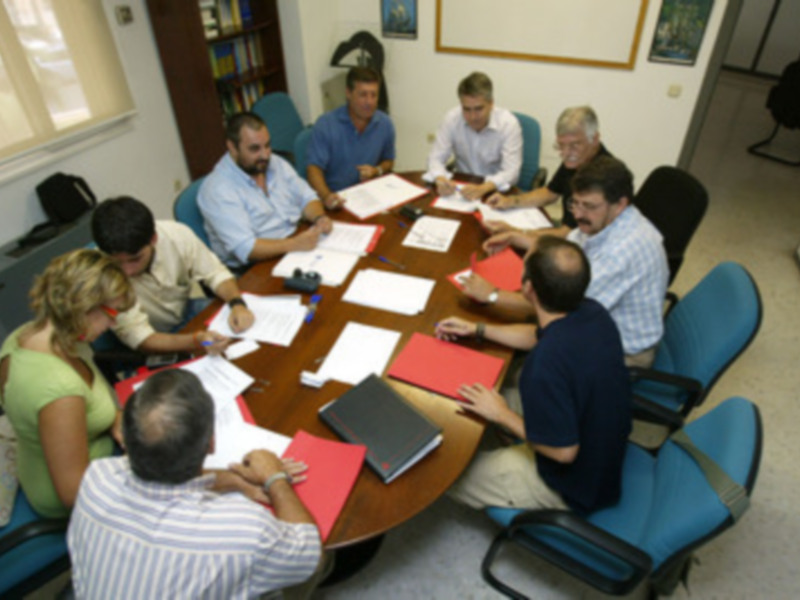 Una reunión de trabajo en un espacio de oficina con varios miembros de la empresa sentados en una mesa redonda, discutiendo y trabajando en documentos.