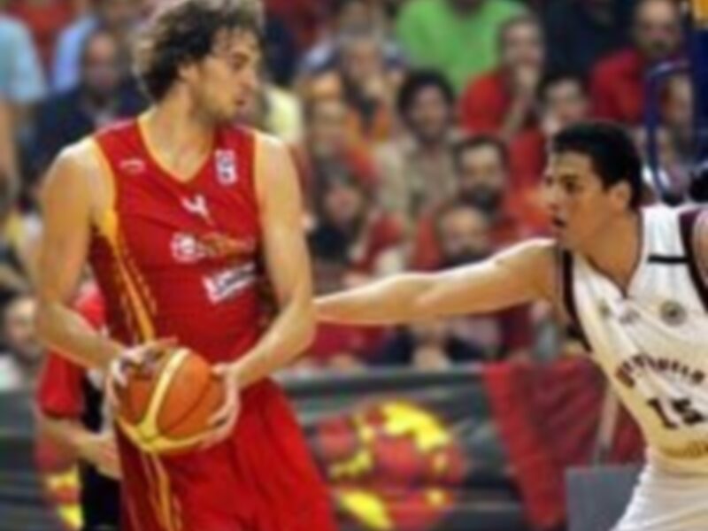 Jugadores de baloncesto en acción durante un partido, uno en rojo y otro en blanco, con el balón en juego.