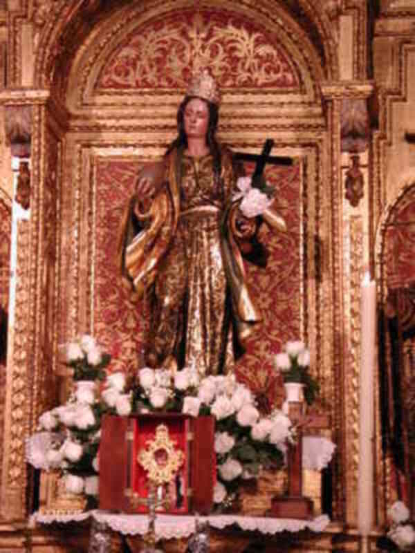 Elegante estatua de una santa vestida de oro, con un cetro y una corona, en un altar adornado con flores y un relieve en el fondo.