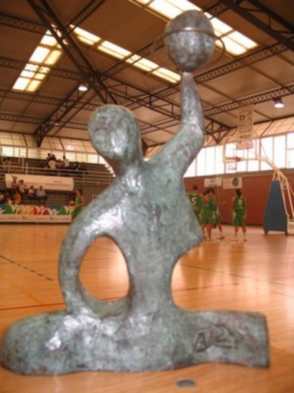 Escultura abstracta de un jugador de baloncesto en una cancha deportiva.