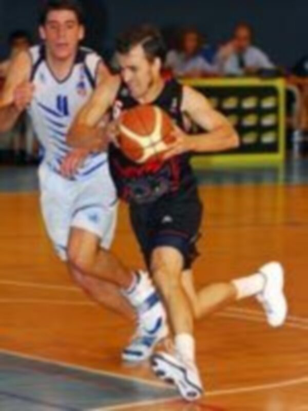 Jugadores de baloncesto en acción durante un partido, uno en blanco y otro en negro, en un entorno deportivo iluminado.