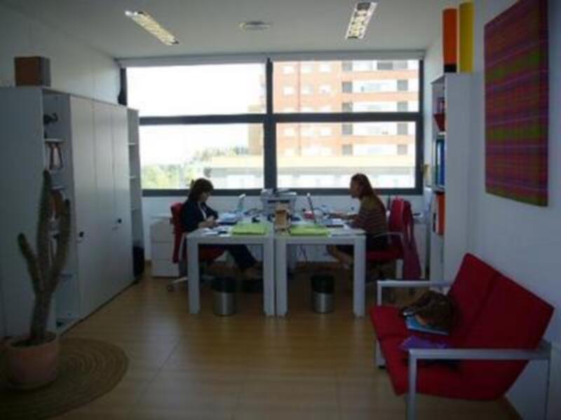 Oficina moderna con dos personas trabajando en un escritorio, decoración minimalista y vista a edificios.